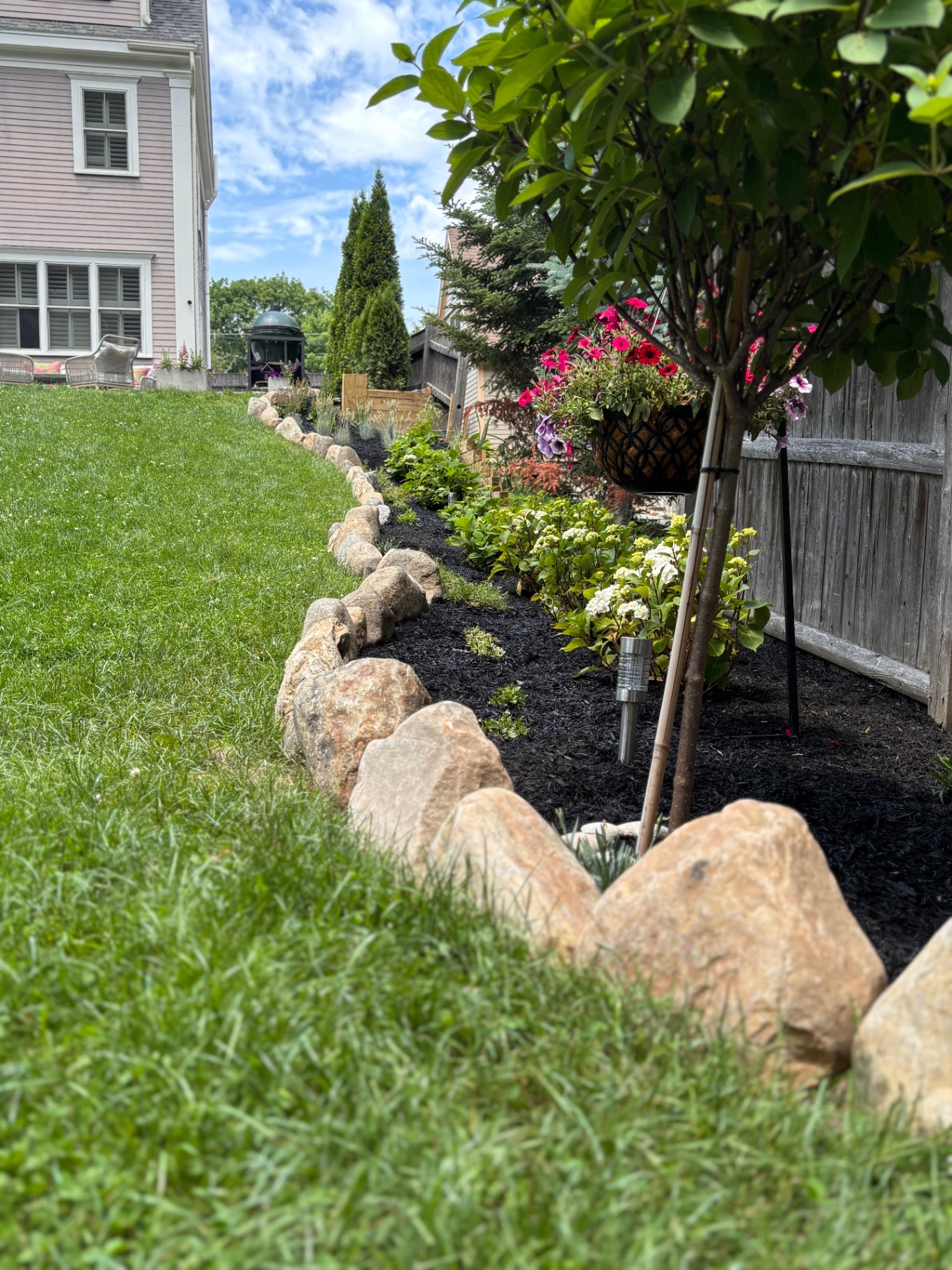 Curved stone-edged garden border with hydrangeas and flowering trees